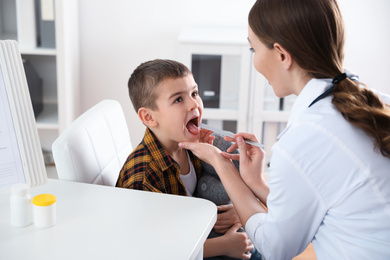 Photo of Children's doctor examining little patient's throat in clinic