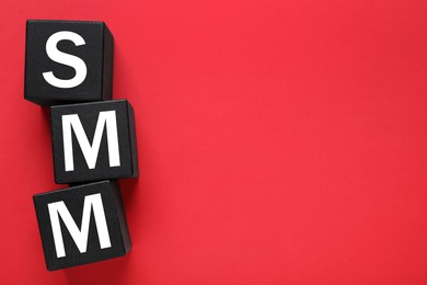 Black cubes with abbreviation SMM (Social media marketing) on red background, flat lay. Space for text