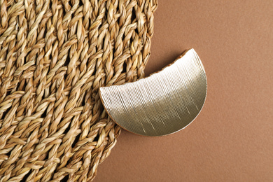 Stylish hair clip and wicker mat on brown background, top view
