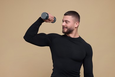 Photo of Handsome sportsman exercising with dumbbell on brown background