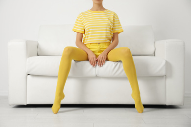 Photo of Woman wearing yellow tights sitting on sofa indoors, closeup