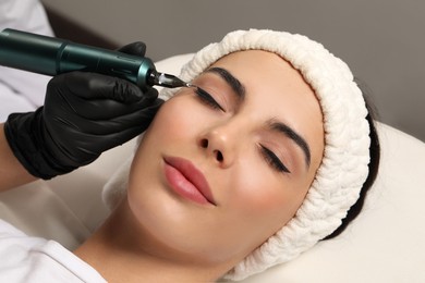 Young woman undergoing procedure of permanent eyeliner makeup on grey background, closeup