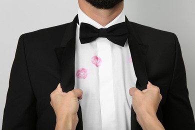 Woman grabbing her husband by suit jacket due to lipstick kiss marks on his shirt, closeup