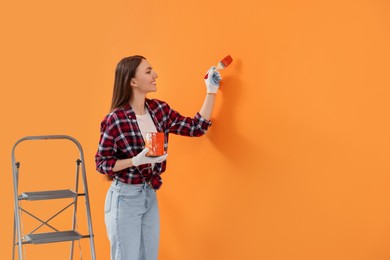 Photo of Designer painting orange wall with brush, space for text