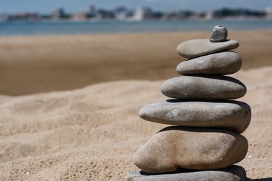Photo of Stack of stones on beautiful sandy beach near sea, closeup. Space for text