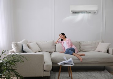 Young woman resting under air conditioner on white wall at home