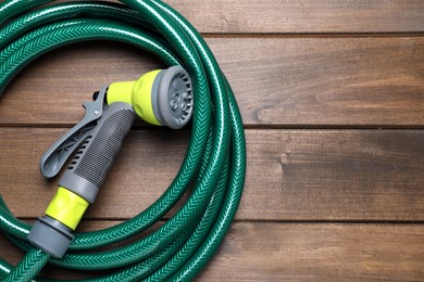 Green garden hose with spray gun on wooden table, top view. Space for text