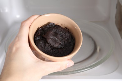Photo of Woman taking ramekin with tasty chocolate pie out of microwave, closeup. Cooking cake
