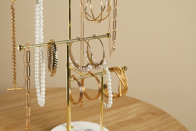 Holder with set of luxurious jewelry on wooden table near beige wall, closeup. Space for text