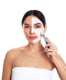 Young woman applying cleansing mask on face against white background