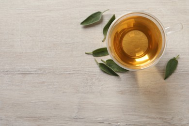 Photo of Glass cup of sage tea and green leaves on wooden table, top view. Space for text