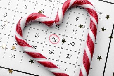Saint Nicholas Day. Heart shape frame of candy canes and confetti on calendar with marked date December 19, flat lay