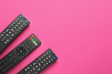 Remote controls on pink background, flat lay. Space for text