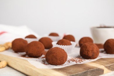 Delicious chocolate truffles powdered with cocoa on wooden board, closeup. Space for text