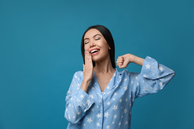 Beautiful Asian woman in pajamas yawning on blue background. Bedtime