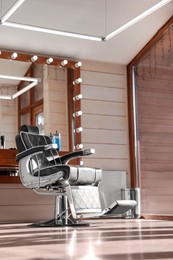 Photo of Stylish hairdresser's workplace with professional armchair and large mirror in barbershop, low angle view. Interior design
