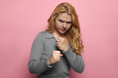 Angry young woman ready to fight on pink background