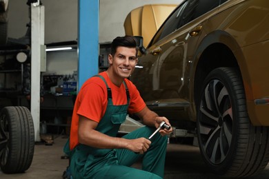 Portrait of professional mechanic with tire wrench near car at automobile repair shop