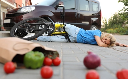 Woman fallen from bicycle after car accident and scattered vegetables on street