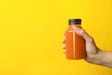 Woman holding bottle of carrot juice on color background, closeup with space for text