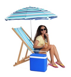 Happy young African American woman with bottle of beer resting in deck chair near cool box on white background