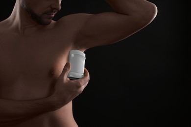 Man applying deodorant on black background, closeup. Space for text