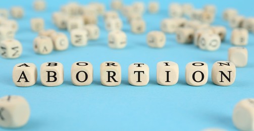 Word Abortion made of wooden cubes on light blue background, closeup