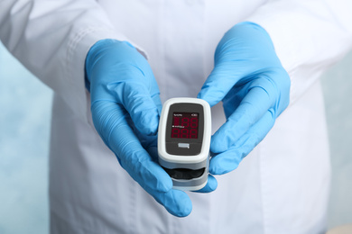 Photo of Doctor holding modern fingertip pulse oximeter, closeup