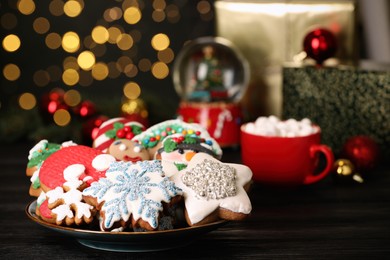 Sweet Christmas cookies and decor on black wooden table against blurred festive lights