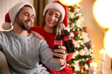 MYKOLAIV, UKRAINE - JANUARY 27, 2021: Young couple holding bottles of Coca-Cola at home, focus on hands. Christmas atmosphere