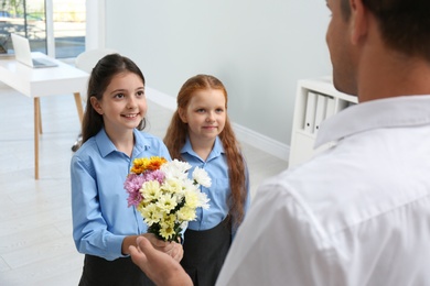 Schoolgirls congratulating their pedagogue with bouquet in classroom. Teacher's day