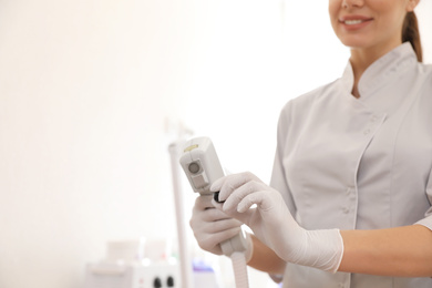 Photo of Young woman holding professional laser epilator in beauty salon, closeup. Space for text