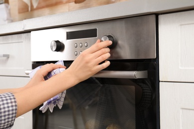 Photo of Young woman adjusting oven settings in kitchen, closeup
