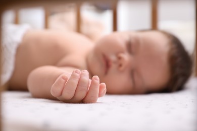 Photo of Cute little baby sleeping in crib at home, focus on hand. Bedtime