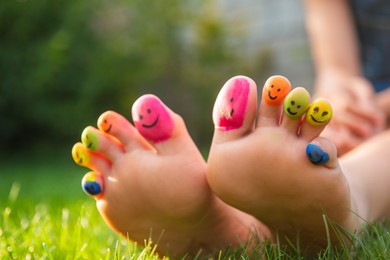 Photo of Teenage girl with smiling faces drawn on toes outdoors, closeup
