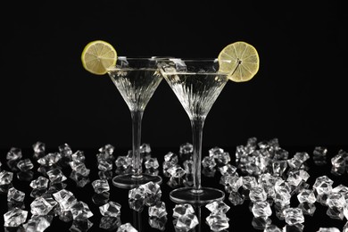 Photo of Two glasses of Martini cocktail and ice cubes on black background