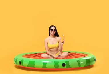 Photo of Happy young woman with sunscreen bottle on inflatable mattress against orange background. Seasonal suntan