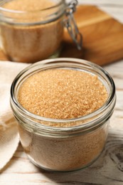 Photo of Glass jar with brown sugar on white wooden table, closeup
