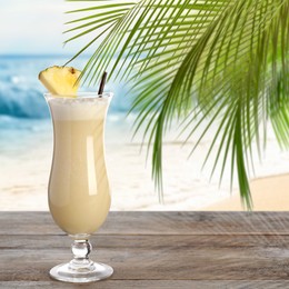 Tasty Pina Colada cocktail on wooden table near ocean. Space for text