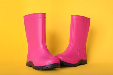 Pair of bright pink rubber boots on pale orange background