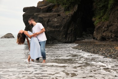 Photo of Happy young couple dancing on beach near sea, space for text