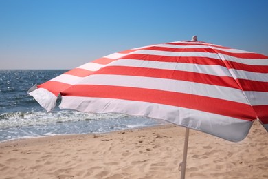 Red and white striped beach umbrella on sandy seashore