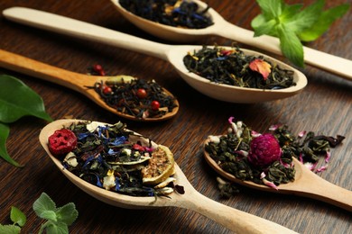 Photo of Spoons with dried herbal tea leaves and fruits on wooden table, closeup