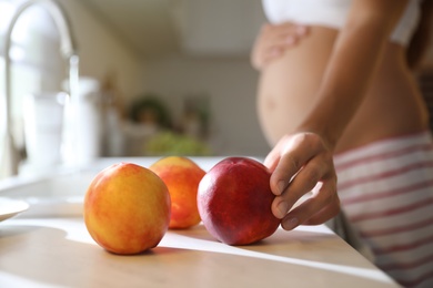 Young pregnant woman washing fresh sweet peaches in kitchen, closeup. Taking care of baby health