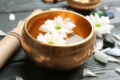 Golden singing bowl with flowers and mallet on grey wooden table, closeup. Sound healing