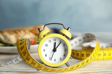 Alarm clock and measuring tape on white wooden table. Diet regime
