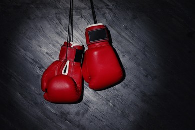 Pair of red boxing gloves hanging in spotlight on grey stone background. Space for text