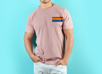 Young man wearing pink t-shirt with image of LGBT pride flag on turquoise background