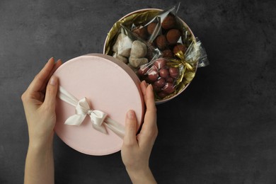 Woman with gift box of chocolate candies and sweets at dark grey table, closeup
