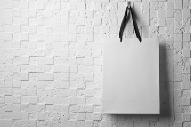 Paper shopping bag with ribbon handles hanging on white wall. Mockup for design